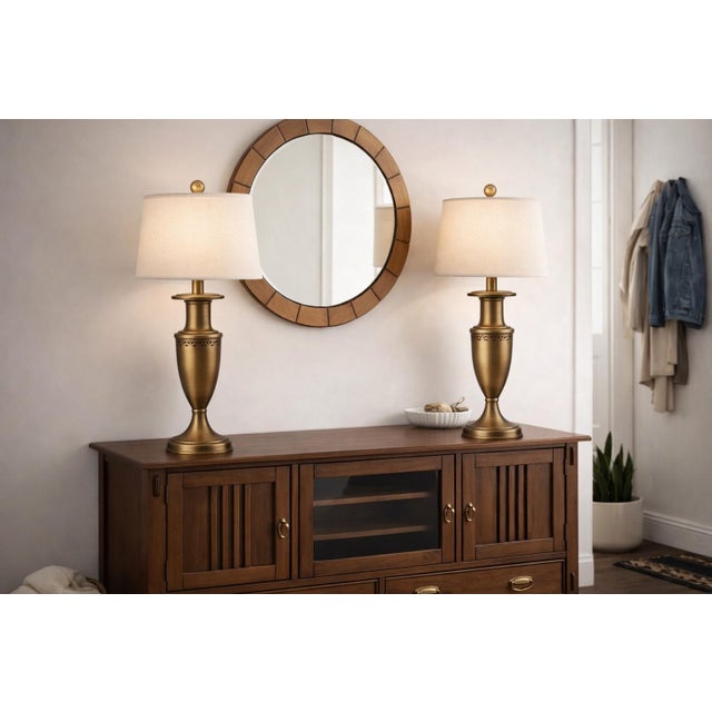 A striking pair of antiqued brass-tone urn table lamps with elegant proportions and refined detailing, newly styled with...