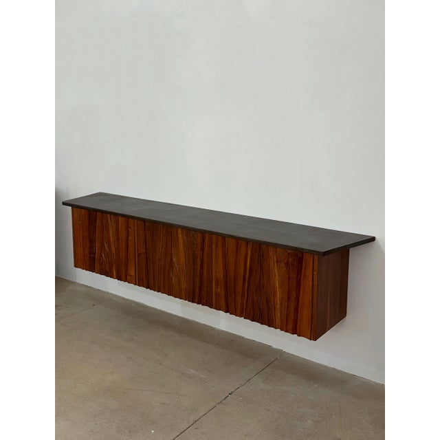 This floating credenza by Gino Russo is characterized by a long, horizontal wall-mounted form with a slate top and a...