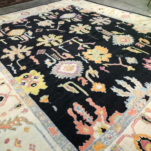 A striking Turkish Oushak rug distinguished by its deep black field and bold, oversized floral and decorative motifs...