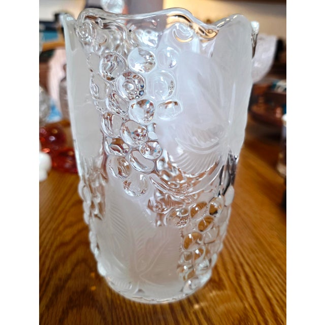 Features a cylindrical body that is decorated with three-dimensional grape clusters and broad grapevine leaves emerging...