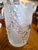 Features a cylindrical body that is decorated with three-dimensional grape clusters and broad grapevine leaves emerging...