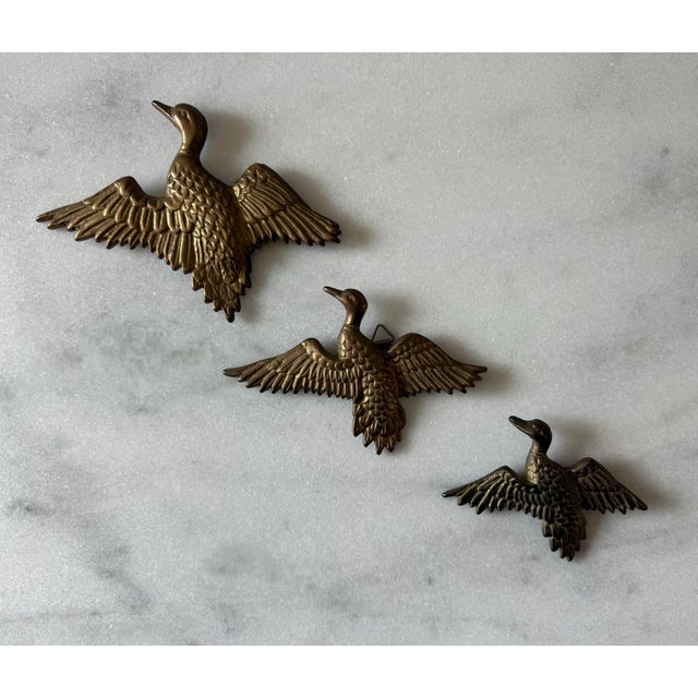 Set of 3 vintage mid century modern brass flying ducks or geese wall plaques. The set features varying sizes and built in...
