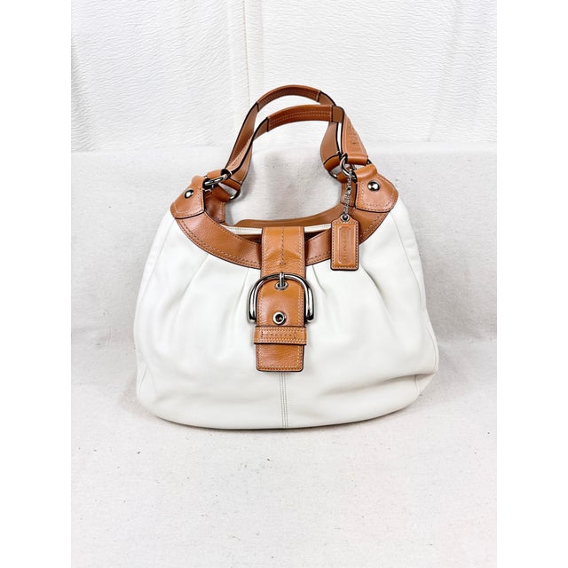 Embrace mid-2000s style with this authentic Coach Soho Lynn Hobo Bag (Style F15075). A beautiful study in contrasting...
