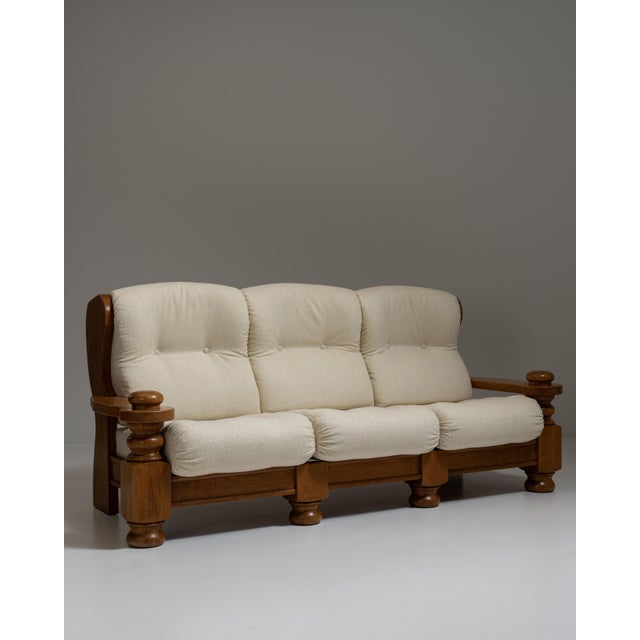 This 1970s Brutalist oak upholstered sofa from France is made in carved oak with cream cushions as a three-seat sofa. The...