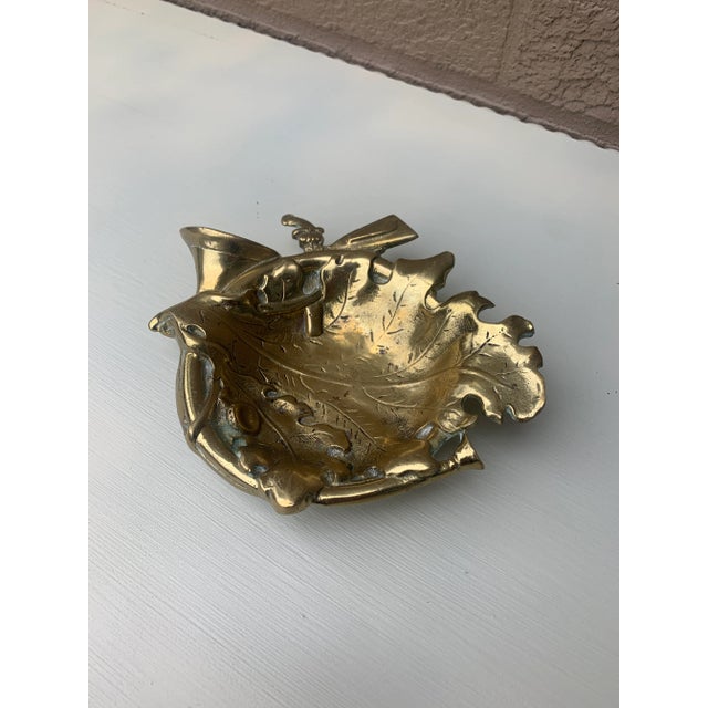 A wonderfully decorative vintage cast brass catchall with a layered hunting composition of horn, pistols, oak leaves, and...