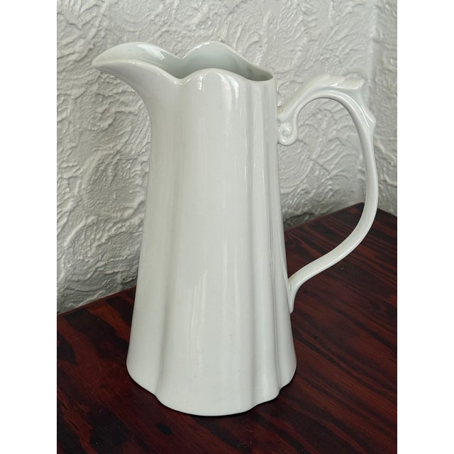 Tall white porcelain pitcher by Godinger with soft scalloped panels. The handle curls into a scroll at the top. Use it for...