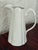 Tall white porcelain pitcher by Godinger with soft scalloped panels. The handle curls into a scroll at the top. Use it for...