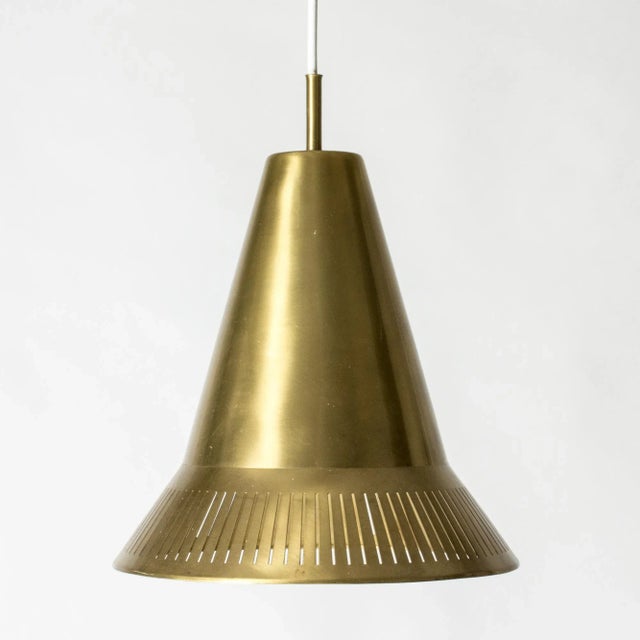 Elegant brass pendant light by Hans Bergström in a hat-like cone shape with perforated stripes around the base. Four...