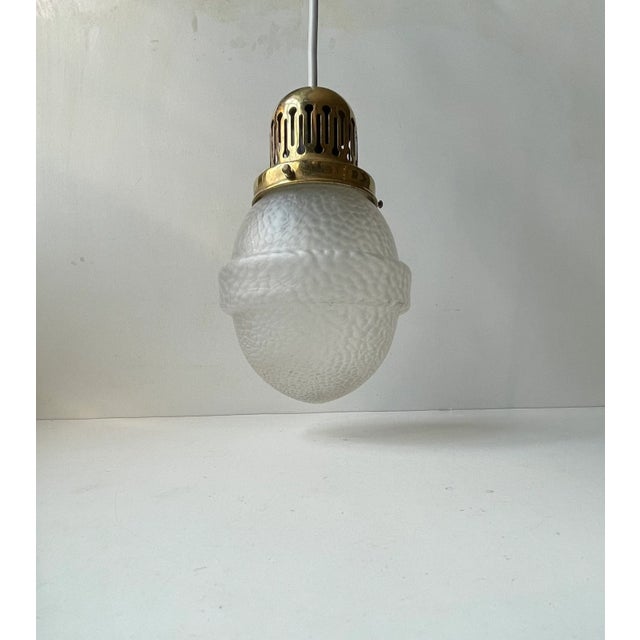 A 1930s ceiling light composed of a partially perforated brass top and a frosted glass shade with lizard skin pattern. It...