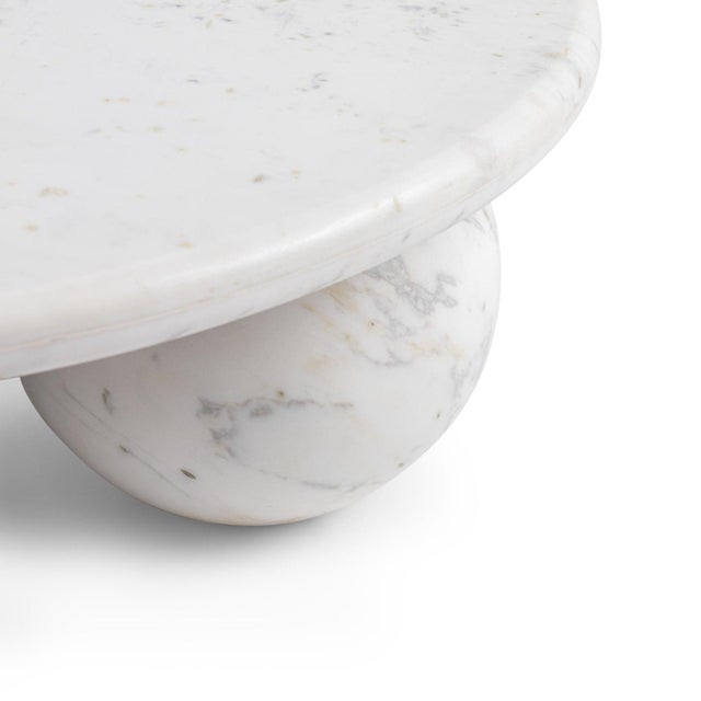 A striking sculptural centerpiece, this round coffee table is crafted entirely from polished white marble and supported by...
