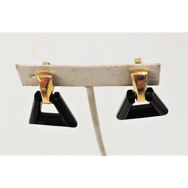 This is part of Chairish’s Costume Jewelry assortment. 1970s goldtone and black Lucite hoop clip back earrings. Marked...