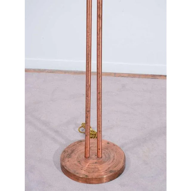 An Art Deco modernist floor lamp in copper. The piece consists of a circular copper base supporting two tubular rods...