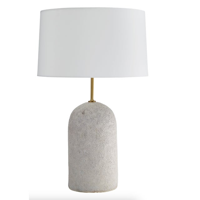 A sleek antique brass iron stem trumpets the half-capsule shape of the ceramic base which features an ivory volcanic glaze...