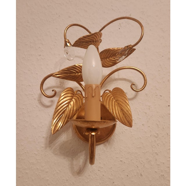Highly decorative, hand-forged wall lamps, gilded with gold leaf, crystal elements, and floral and leaf embellishments....