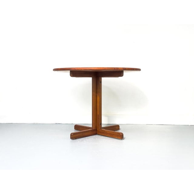 Round, very well-maintained teak dining table with a cross-shaped base. The entire construction is made of solid teak. The...