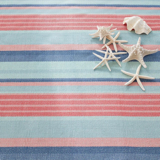 Sun-drenched hues of corals, sky, and grass intersperse with variegated coastal blue deck stripes in this low profile rug....