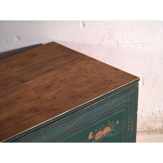 This antique Chinese trunk in green-lacquered elm is a dowry chest with a sliding lid and a floral front on a green...