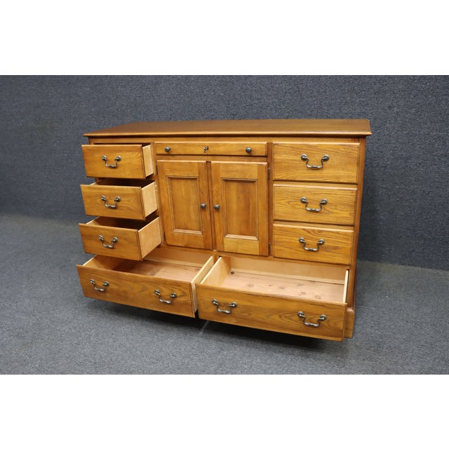 American of Martinsville oak dresser featuring a traditional form with a mix of drawers and center cabinet storage. The...