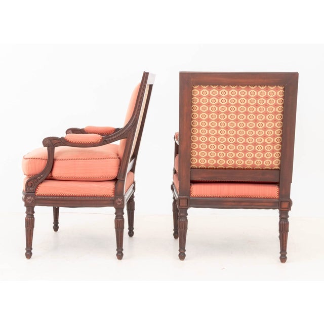 An elegant matched pair of Louis XVI-style stained mahogany armchairs, or fauteuils, combining restrained Neoclassical...