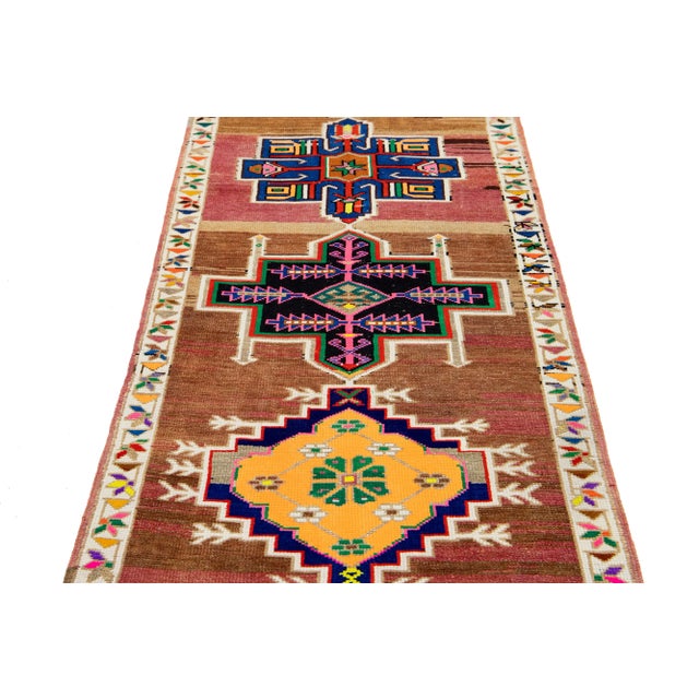 This exquisite vintage runner rug has been meticulously hand-knotted from high-quality wool. It features a rich brown...