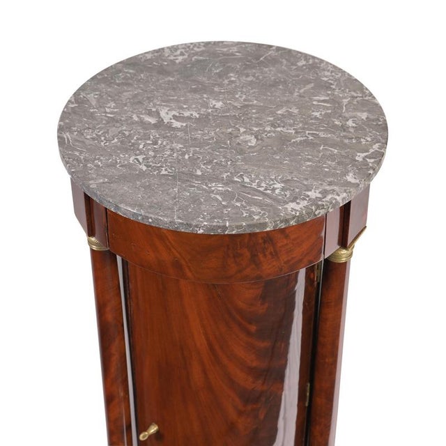 Small barrel-shaped cabinet, France, ca. 1810; pyramid-shaped mahogany with a marble top; four full columns with brass...