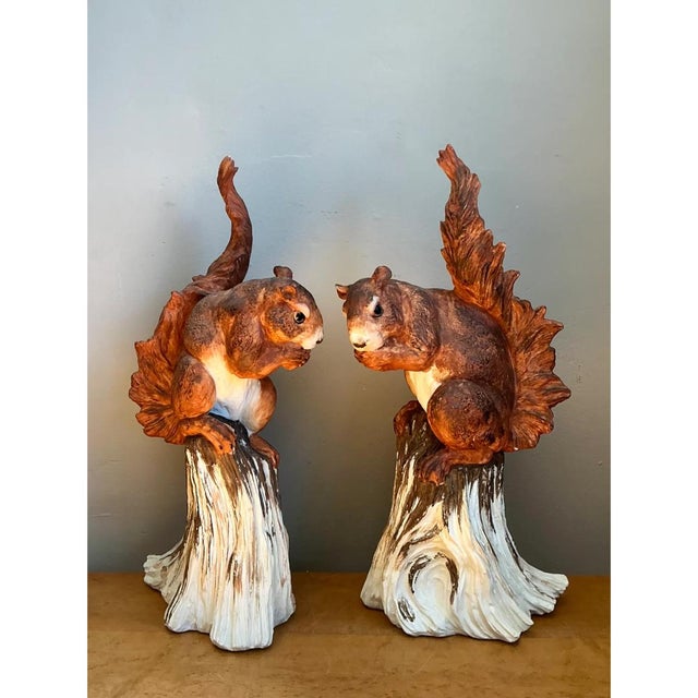 These vintage ceramic figures are a mirrored pair of squirrels, each perched on a tall, tapering tree stump and facing...