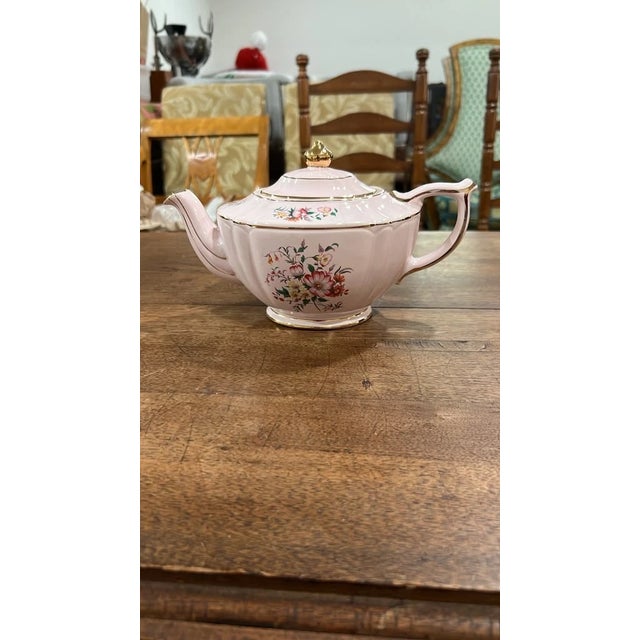 An elegant vintage soft pink porcelain teapot featuring a ribbed, fluted body decorated with vibrant hand-painted wild...