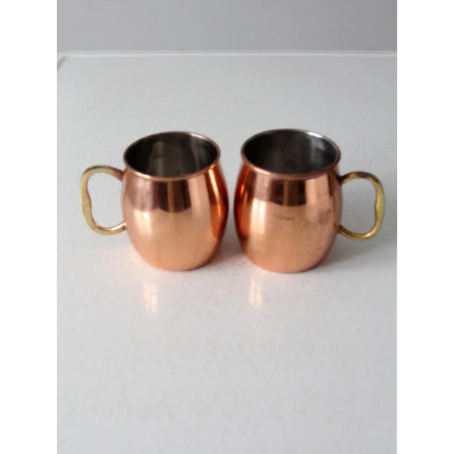 This is a pair of vintage Godinger copper mugs. The Moscow Mule mug set feature stainless steel interiors with brass handles.