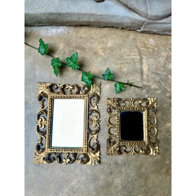 Charming pair of vintage Italian wall mirrors featuring ornate Rococo-inspired scrollwork frames with a rich gold finish....