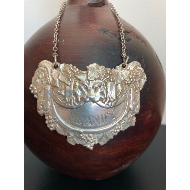 Mid 20th century English silver hanging label for a brandy bottle or decanter. Shown with a lion skin holding the...