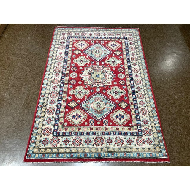 Hand-knotted Pakistani Kazak wool rug featuring a red field with bold geometric medallions and stylized floral motifs in...