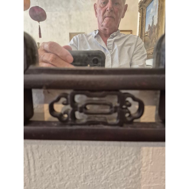 Qing Dynasty Chinese wall mirror handcrafted with a carved mahogany frame around a distressed looking glass.