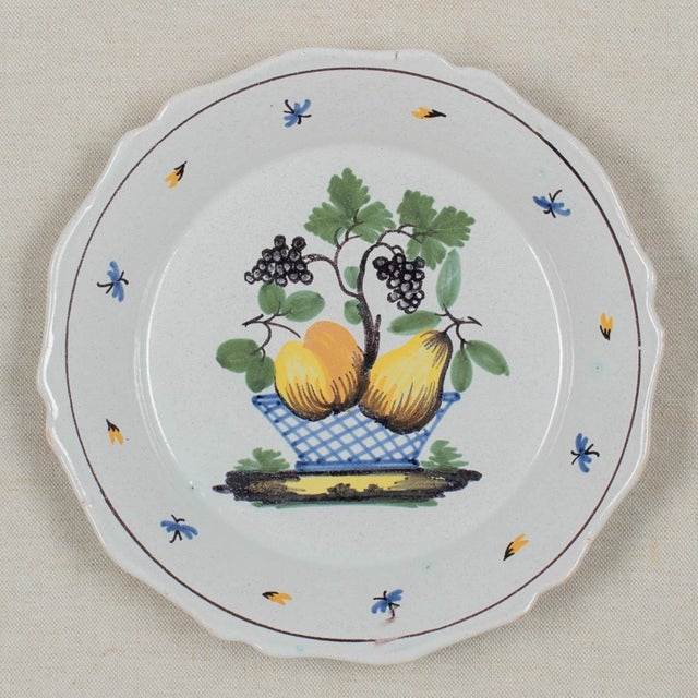 A set of four 18th century French faience plates with primitive hand painted decoration of fruit baskets and grapes, each...