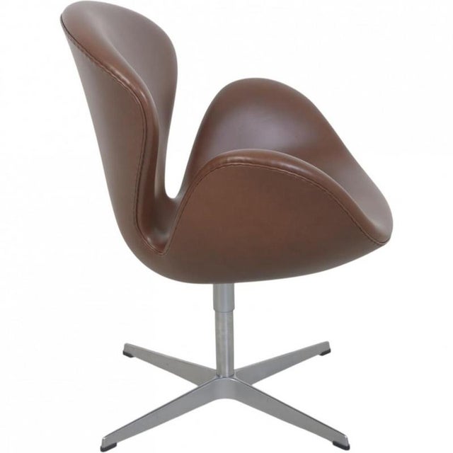 Arne Jacobsen tall Swan chair upholstered in mokka classic semi anilin leather, and with a swivel base of aluminium. The...