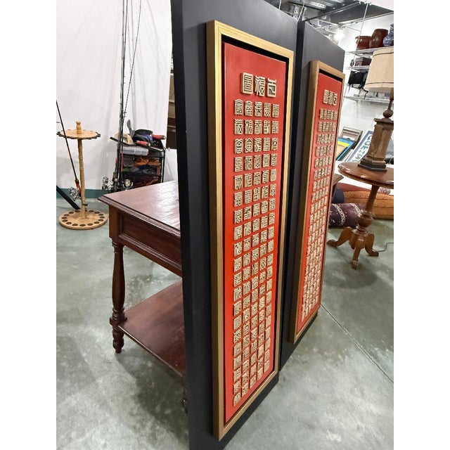 Striking decorative Chinese wall art featuring raised gold characters set against a rich red background. The panel is...