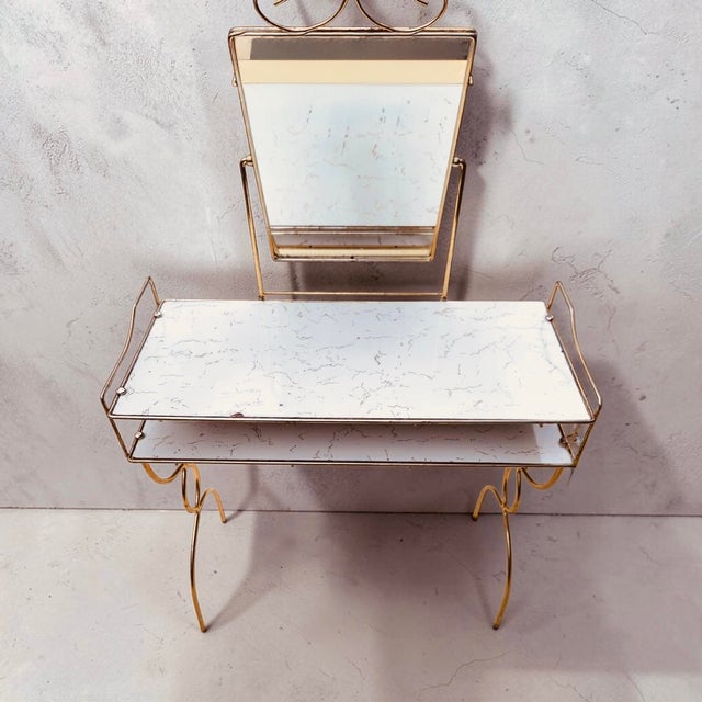 Classic 1970s Hollywood Regency two-tier makeup vanity table featuring an elegant gold-toned scrollwork frame, an...