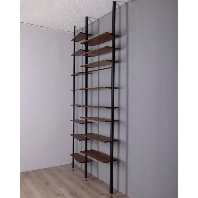 Two-section floor-to-ceiling bookcase, with black metal frame and wooden shelves, gold-plated brass feet and ceiling tips,...