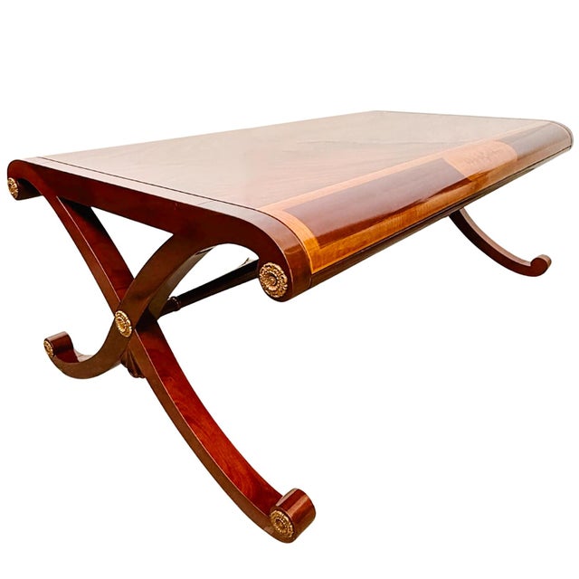 A Neoclassical-style coffee table featuring a stunning book-matched flame mahogany top that creates a mirrored cathedral...