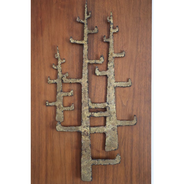 A striking Brutalist wall sculpture of three stylized, tree-like forms in torch-cut brass, mounted on a warm walnut panel....