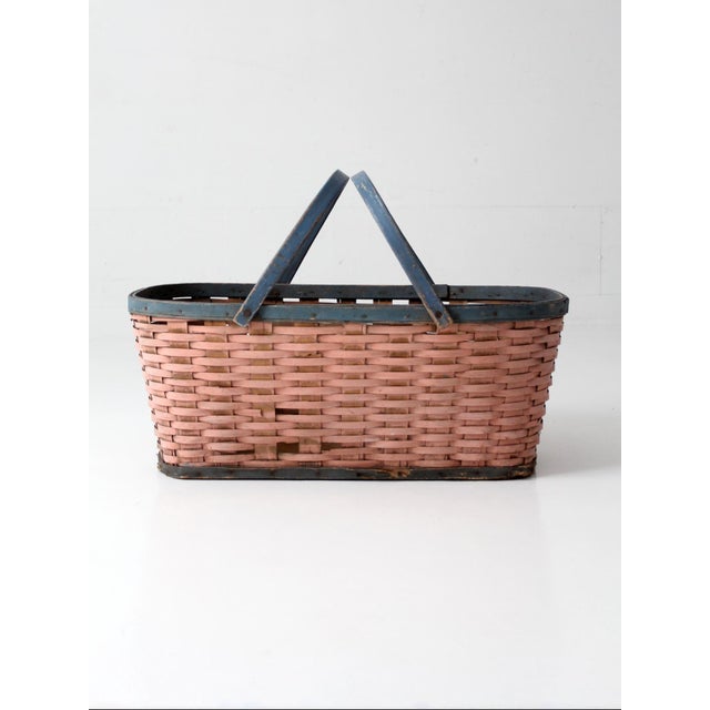 A large early American gathering basket with an elongated oval form and painted splint weave in soft pink with blue-green...