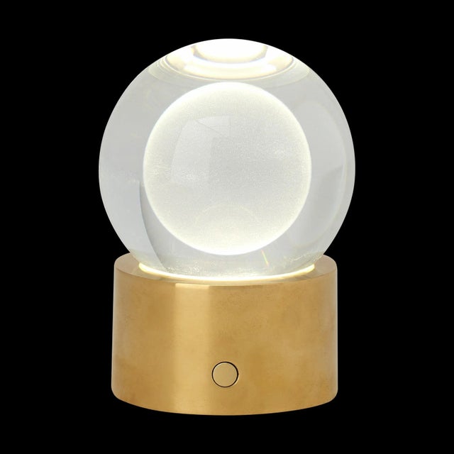 The Mina Rechargeable Table Lamp by Sean Lavin features an elegant sphere of pure optic crystal elegantly resting on a...