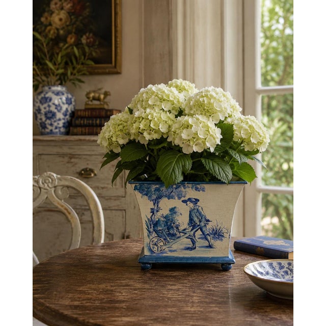 A decorative French Provincial cachepot fashioned from painted tole in a softly aged blue-and-cream palette. Each side is...