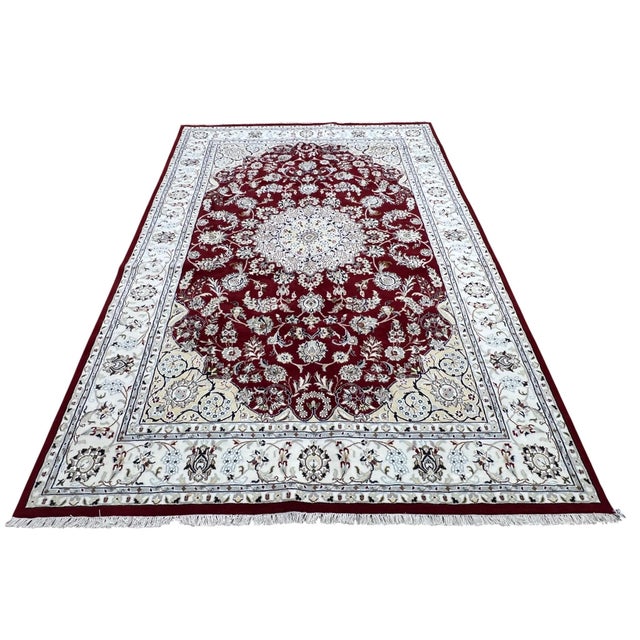 Persian Nain rug, hand knotted in India from 100% wool. Measuring 6’1” x 9’2”, the rug features an elegant central...