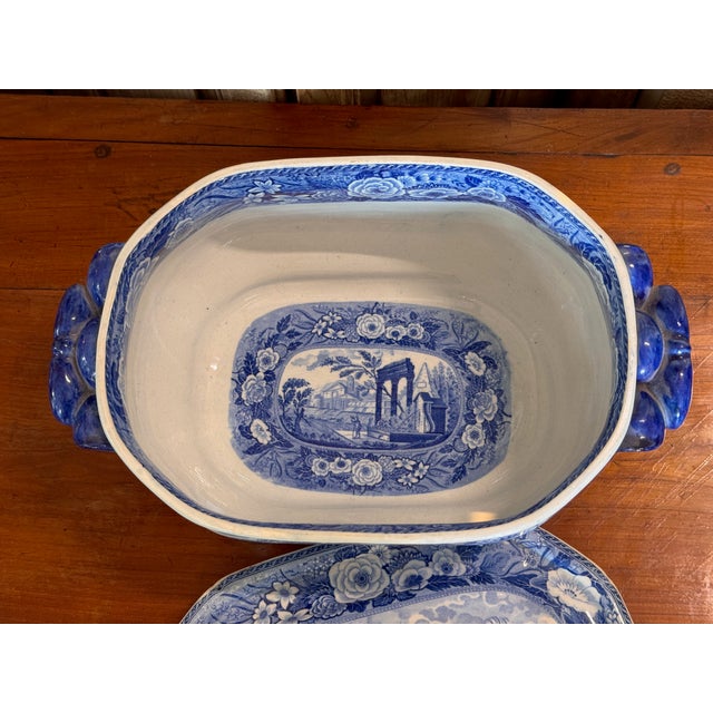 A blue and white transferware soup tureen with its lid. Country scenes all around — a thatched cottage on the body, a...