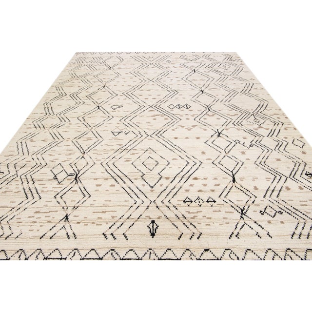 Beautiful modern Moroccan style hand-knotted wool rug with an ivory field. This piece has black and tan accent colors in a...