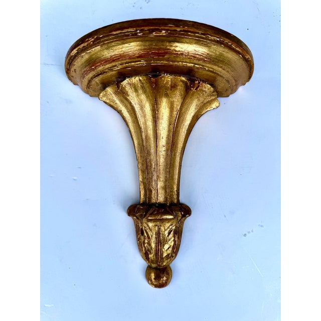 An Italian giltwood wall bracket with a shaped, semicircular shelf above a flared support, acanthus leaf decoration and a...
