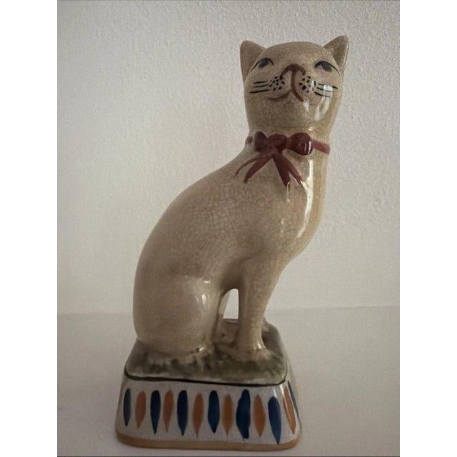 This vintage Staffordshire style cat figurine features a charming design with a red bow and a wry smile, adding a...