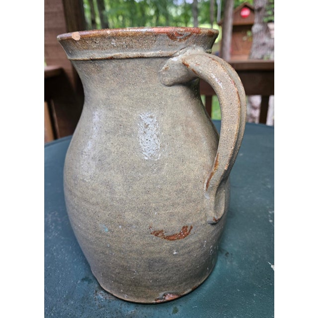 This antique North Carolina salt-glazed stoneware pitcher is attributed to the Craven family of potters. The one-gallon...