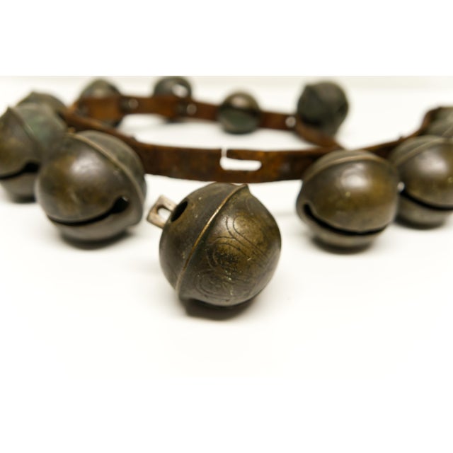 An antique late 19th century set of 13 graduated brass sleigh bells mounted on a leather belt, creating a wonderful...