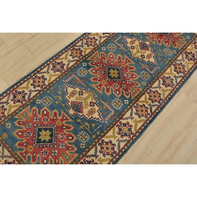 A tribal Caucasian Kazak runner hand-knotted with fine wool on a cotton foundation. This rug features geometric medallions...